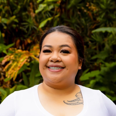 Staff Member With Braces Smiling In Front Of Greenery